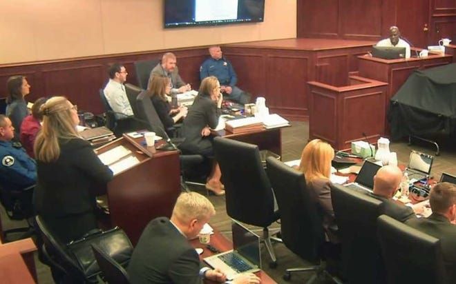 Colorado theater shooter James Holmes, left rear in light-colored shirt, watches during testimony by witness Derick Spruel, upper right, on the second day of his trial in Centennial, Colo., Monday, April 27, 2015. Standing at left is prosecutor Lisa Teesch-Maguire. (Colorado Judicial Department via AP, Pool)