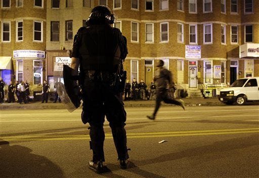 A police officer watches as a man runs down North Avenue as a curfew approaches, Thursday, April 30, 2015, in Baltimore. (AP Photo/Patrick Semansky)