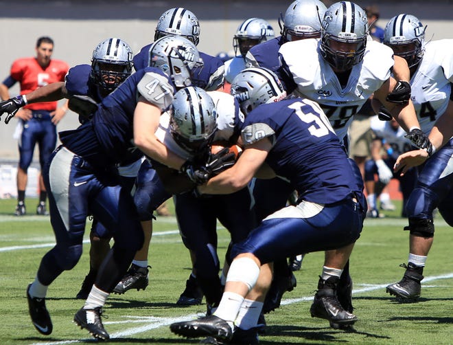 Nick Marino (47) and Jared Kuehl (58) work to bring down Trevon Bryant during UNH's annual Blue/White Spring scrimmage on Saturday.