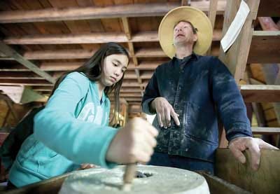 Photo by Jake West / New Jersey Herald Olivia Tomasello, a fifth-grader at Evergreen Community Charter School in Cresco, Pa., grinds corn under the supervision of the Millbrook miller, Scott Dutton, at Millbrook Village.