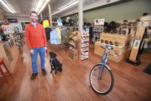 Jerred Roberts stands with his dog Buddy inside of his store Puzzle Creek Outdoor in Forest City. He will open a second location in uptown Shelby July 6.