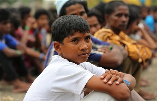In this Friday, May 22, 2015, Atau Rahman, center, sits with Rohingya migrants at a temporary shelter in Bayeun, Aceh Province, Indonesia. Rahman, 12, of Sittwe, told the Associated Press he was kidnapped. Rahman said he and nine other boys were grabbed by a "weird man" and shoved onto a boat where they simply disappeared. They were held for weeks offshore until enough bodies were crammed into the ship to leave. (AP Photo/Tatan Syuflana)