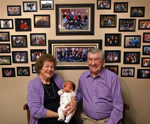 In this April 17, 2015 photo, Leo and Ruth Zanger sit with their 100th grandchild, Jaxton Zanger, in Leo's real estate office in Quincy, Ill. Jaxton was born April 8 to parents Austin and Ashleigh Zanger. For the numerically inclined, Jaxton was also No. 46 among the great-grandchildren. The Zangers also have 53 grandkids and one great-great-grandchild for a nice round 100. "The good Lord has just kept sending them," Leo Zanger said of the grandkids. "We could start our own town." (Phil Carlson/The Quincy Herald-Whig via AP)