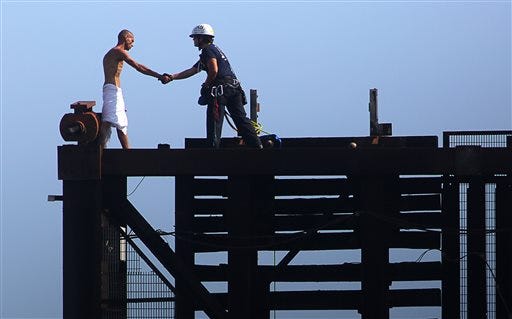 A member of the Fort Lauderdale Fire Rescue Tactical Rescue Team rescues a naked man on top of a raised drawbridge on Friday, May 22, 2015 in Fort Lauderdale, Fla. Witnesses said the unidentified man was swimming in the river earlier and was walking across the railroad bridge Friday morning when it began to rise, forcing him to scamper to the top. (Michael Clary/South Florida Sun-Sentinel via AP)
