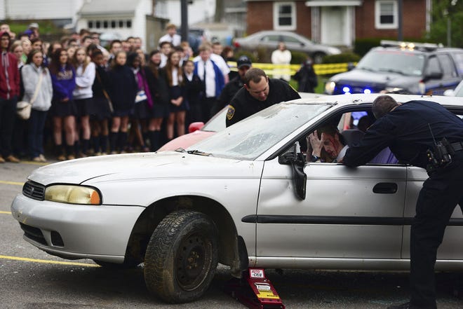 Our Lady of the Sacred Heart High School students look on as a Coraopolis police officer checks on senior Zach Lander, who participated in a mock crash program earlier this month. In the two-car crash scenario, Zach was texting while he was driving. Teenage traffic fatalities have historically increased between Memorial Day and Labor Day, and AAA East Central has dubbed summer the "100 Deadliest Days" for young drivers.
