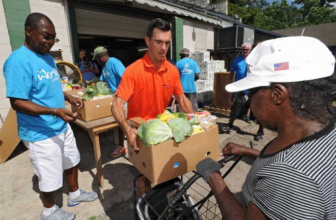 Bob.Mack@jacksonville.com Billy Horschel (center) hands a box of food to one of the people waiting in line as volunteer J.B. Bryant (left) watches during a charity event for Feeding Northeast Florida on Friday at The Worship Center of Jacksonville.