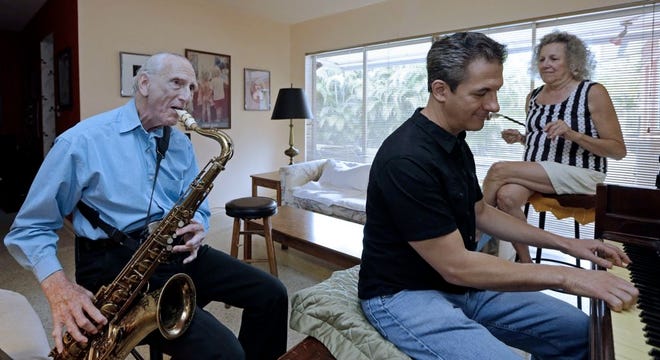 Al Karp, left, plays the saxophone as he rehearses with his son Larry, center, and wife Saundra, right, at their home in North Miami Beach. The trio performs old standards locally to ease stress and help raise money to save their home from foreclosure.