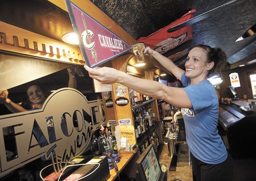 Kendra Falcone, owner of Falcone's Tavern with her husband, Greg, proudly hangs a Cavaliers pennant in their Perry Township bar and grill Wednesday in preperation for Game 1 of the NBA Finals tonight.