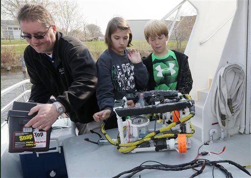 In a photo from Thursday, May 7, 2015 in Alpena, Mich., fifth grade teacher Bob Thomson helps students with their homemade machine designed to release trout on a artificial reef in Lake Huron. (AP Photo/Carlos Osorio)