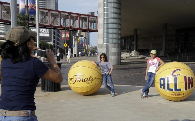 In this photo taken, Friday, June 5, 2015, Laurice Moore takes a photo of daughters, Elizabeth, 8, and Emma, 11, in front of Quicken Loans Arena in Cleveland. Behold a new, shining Cleveland, once dubbed the Mistake on the Lake. Well, times have changed, and so have the attitudes of skeptical and cynical Cleveland fans, many of whom grew up hoping for the best, expecting the worst and agonizing through moments that have earned dubious nicknames: Red Right 88, The Drive, The Fumble, The Shot, The Move, The Decision. One man has transformed this town. LeBron James has Cleveland believing.