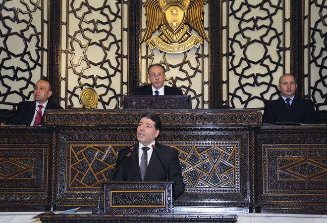 In this photo released by the Syrian official news agency SANA, Syrian Prime Minister Wael al-Halqi, center front, speaks during a parliament session in Damascus, Syria, Monday, June 8, 2015. Al-Halqi called on young Syrians Monday to fulfill their mandatory military service obligation, promising better pay for troops on the front lines as well as one meal of hot food a day. (SANA via AP)
