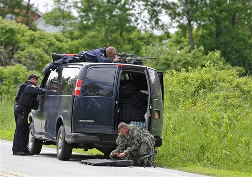 A law enforcement agent looks through a sniper scope while another in camouflage assembles a weapon during a search for two escaped killers in Boquet Tuesday