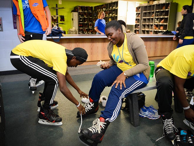 Jamila Alexander, from Trinidad and Tobago, helps lace up the skates of Kassinda Prescod's, from St. Vincent, on Saturday at the Sports and Social Impact Festival at the Ellenton Ice and Sports Complex.