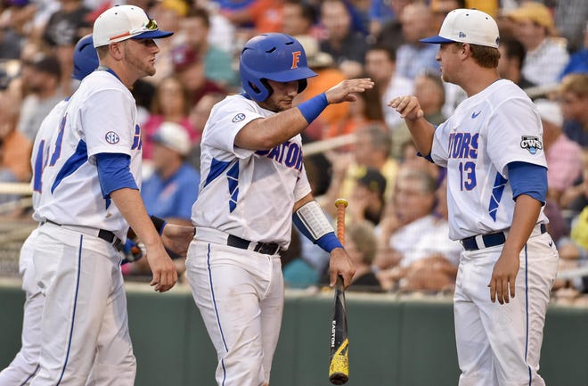 Florida's Mike Rivera, center, is greeted by Kirby Snead (13) and Mike Fahrman, left, after he scored on a single by Ryan Larson during the fourth inning of an NCAA College World Series baseball game against Miami in Omaha, Neb., Saturday, June 13, 2015.