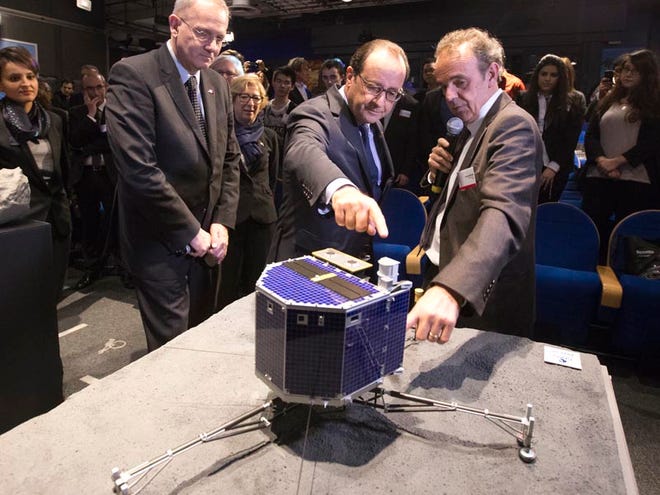 In this Wednesday, Nov. 12, 2014 file photo, French President Francois Hollande, center, with French astrophysicist Francis Rocard look at a model of Rosetta lander Philae, as they visit the Cite des Sciences at La Villette in Paris during a broadcast of the Rosetta mission as it orbits around comet 67/P Churyumov-Gersimenko. The European Space Agency says its comet lander Philae has woken up from hibernation. The probe became the first spacecraft to land on a comet when it touched down on the surface of 67P in November. The German Aerospace Center, which operates Philae, said Sunday, June 14, 2015 that the probe communicated with the ground team on Earth for 85 seconds late Saturday.