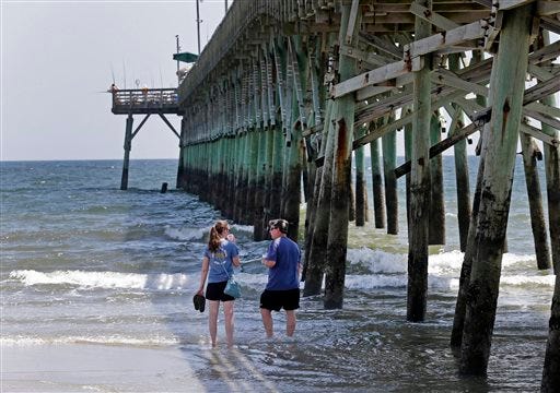 Doug Baucom, right, of Wadesboro, talks with his daughter Katie Reynolds, left, of Boone, N.C., as they stand in the surf by the Ocean Crest Pier in Oak Island, N.C., Monday, June 15, 2015. Beachgoers cautiously returned to the ocean Monday after two young people lost limbs in separate, life-threatening shark attacks in Oak Island on Sunday. (AP Photo/Chuck Burton)