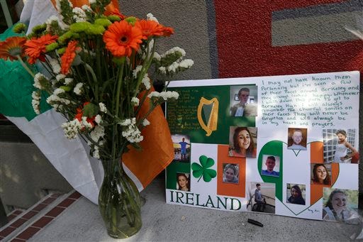 A flag of Ireland, flowers and a sign are shown at a shrine left for victims of the Library Gardens apartment building balcony collapse Wednesday, June 17, 2015. The balcony broke loose from the building during a 21st birthday party early Tuesday, killing several people and seriously injuring others. (AP Photo/Jeff Chiu)