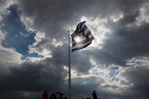 Tourists stand beneath a Greek flag fluttering against the sun at the ancient Acropolis hill , in Athens, on Monday June 22, 2015. A top European Union official said that debt talks between Greece and its international creditors have made some progress but that a deal to avoid potential bankruptcy remains elusive. (AP Photo/Petros Giannakouris)