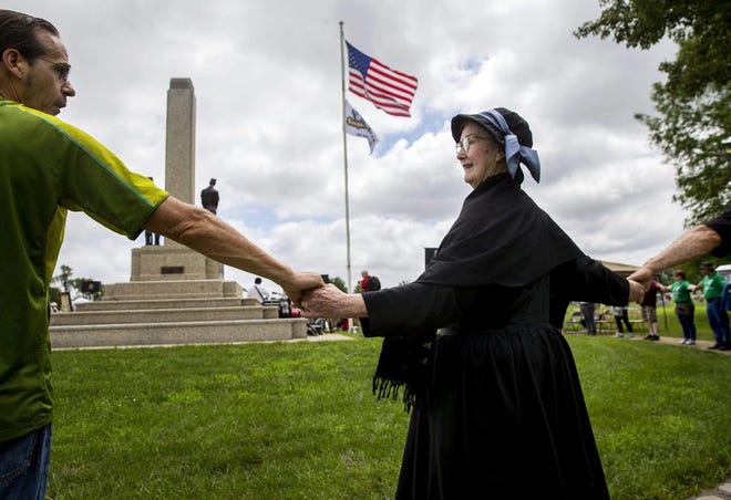Margaret Orner of Glen Mills, Pa., portraying labor and community organizer Mother Jones, grasps hands with Kevin Clarke of Mt. Olive as people circle around the Mother Jones Monument at Union Miners' Cemetery in Mt. Olive during a rededication ceremony Saturday, June 20, 2015.
