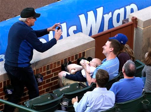 In this photo taken Tuesday, June 23, 2015, baseball fan Keith Hartley, center, is photographed by another fan, after he caught a foul ball while bottle-feeding his 7-month-old son during the second inning of baseball game between the Chicago Cubs and the Los Angeles Dodgers at Wrigley field in Chicago. (Nuccio DiNuzzo/Chicago Tribune via AP)
