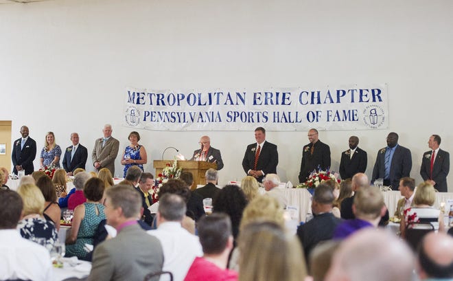 Master of ceremonies John Leisering introduces the 2015 inductees of the Erie Metropolitan Chapter of the Pennsylvania Sports Hall of Fame during the hall of fame dinner held at the Zem Zem Shrine Club on June 23 in Millcreek Township. Inductees and inductee representatives pictured to the left of the podium are, from left: John Gordon, father of inductee Sheena Gordon, McDowell track & field alumna; Becky Berzonski Ogden, North East and University of North Carolina-Wilmington golf team alumna; Rick Gotkin, Mercyhurst University men's hockey coach; Jim Vogt, Iroquois football coach and administrator; and Sarah Lunger, widow of posthumous inductee Joe Lunger, a longtime Villa Maria baseball and basketball coach. Pictured to the right of the podium from left to rigt are: Mike Mischler, Cathedral Prep football head coach; Ed Hinkel, a former football player at Cathedral Prep and the University of Iowa; Rod Jones, brother-in-law of inductee Bob Sanders, also a former football player at Cathedral Prep, the University of Iowa and the NFL's Indianapolis Colts; Mo Troop, East High School football coach and representative of inductee Jovon Johnson, a former football player at Mercyhurst Prep who is currently with the Canadian Football League's Ottawa Redblacks; and Dave Hewett, standout Erie bowler and golfer. ANDY COLWELL/