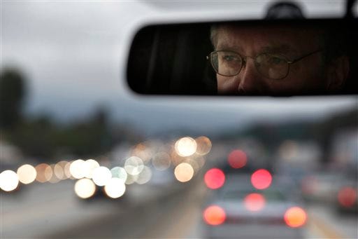 In this Friday, May 22, 2015 photo, UCLA employee and volunteer vanpool driver Fredrick Merrick, who commutes 80 miles each way from Moreno Valley, Calif., to the Westwood section of Los Angeles, is reflected in the rear view mirror as he drives a 12-passenger van through traffic on his way back home near Los Angeles. Within 30 years, the Department of Transportation projects, drivers will have to tolerate stop-and-go conditions or slow traffic for some period of each day on more than a third of U.S. highways. (AP Photo/Jae C. Hong)