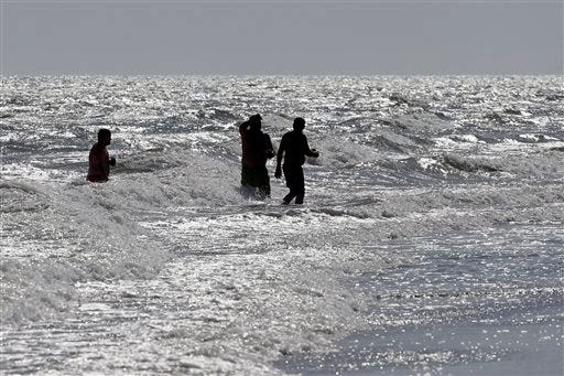Vacationers walk in the surf in Oak Island, N.C., Monday, June 15, 2015, the day after a 12-year-old girl from Asheboro lost part of her arm and suffered a leg injury, and a 16-year-old boy from Colorado lost his left arm about an hour later and 2 miles away in two separate shark attacks off Oak Island. (AP Photo/Chuck Burton)