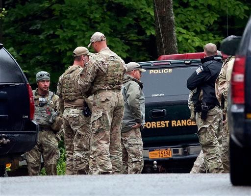 Law enforcement officers gather on a road on Sunday, June 28, 2015, in Malone, N.Y. The shooting death of one escaped killer brought new energy to the three-week hunt for a second escaped murderer in the United States as helicopters, search dogs and hundreds of law enforcement officers converged on a wooded area 30 miles from Clinton Correctional Facility. (AP Photo/Mike Groll)