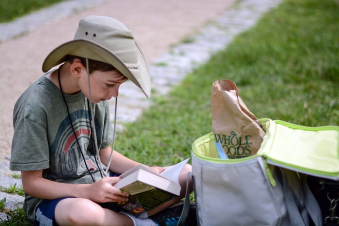 Matthew Lubarsky takes some time to read while waiting for a fish to bite during the annual fishing derby for kids, organized by experienced fisherman Jerome Moisand, at Spy Pond Park in Arlington, June 27, 2015.  (Wicked Local Photo/James Jesson)