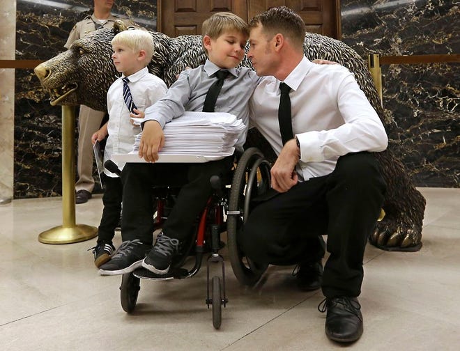Otto Coleman, 6, waits outside the Governor's office with his brother Fenton, 4, left, and father Joshua, to deliver a stack of petitions with thousands of signatures calling on California Gov. Jerry Brown to veto a measure requiring nearly all California school children to be vaccinated Monday, June 29, 2015, in Sacramento, Calif. The state Senate approved the bill sending it to Brown. Joshua Coleman said his son has been wheelchair bound as a result of an adverse reaction to a vaccine. (AP Photo/Rich Pedroncelli)