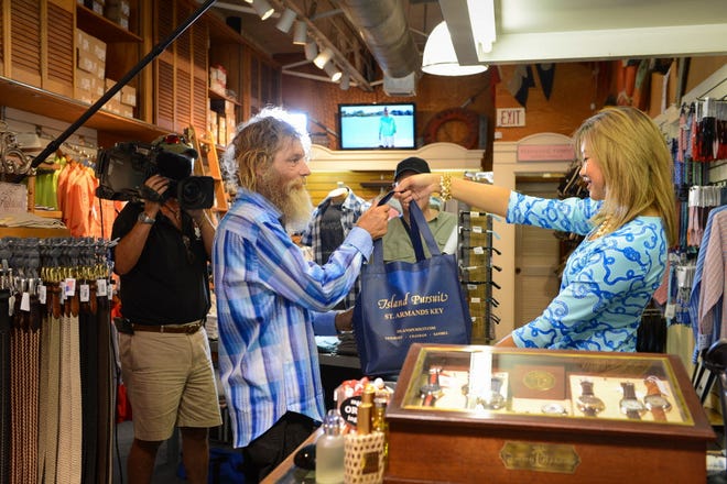 Patra Jordan hands Donald Gould a bag filled with new clothes from Island Pursuit as Inside Edition films him for a Monday segment.