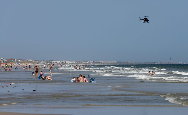 A helicopter flies close to the water as vacationers relax on the beach in Oak Island on Monday, June 15, 2015. A 12-year-old girl from Asheboro lost part of her arm and suffered a leg injury, and a 16-year-old boy from Colorado lost his left arm about an hour later and 2 miles away in two separate shark attacks late Sunday afternoon.
