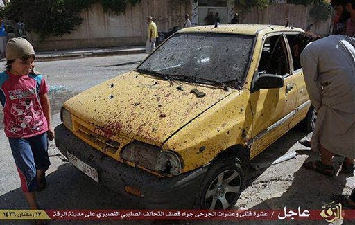 This Saturday, July, 4, 2015 photo provided by a website of the Islamic State group, shows people inspecting a car purportedly damaged by U.S.-led airstrikes on Raqqa, Syria. A series of U.S.-led coalition airstrikes targeting the Islamic State group's stronghold of Raqqa in eastern Syria has killed at least 10 militants and wounded many others. The airstrikes were confirmed by the coalition, Raqqa-base activists and the Islamic State group. Arabic on banner reads, "Raqqa Urgent / Ten killed and tens wounded by crusader (Christian)-Nusayri (Alawite) coalition on Raqqa city. 17 Ramadan 1436 Hijri." (Islamic State militant website via AP)