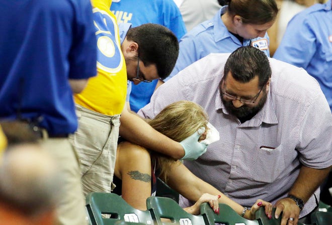 In this Monday, July 6, 2015, photo, a fan is helped after being hit by a foul ball during the ninth inning of a baseball game between the Milwaukee Brewers and the Atlanta Braves in Milwaukee. (AP Photo/Morry Gash)