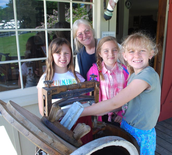 Third-graders from the Paul School in Wakefield, New Hampshire, learn how to wash laundry, 19th Century style, during a field trip to Willowbrook Museum in Newfield in June. From left are Ava Debrico, Willowbrook employee Johanne Vaters, Hailey Belliveau, and MaKayla MacDonald. PHOTO BY CJ PIKE