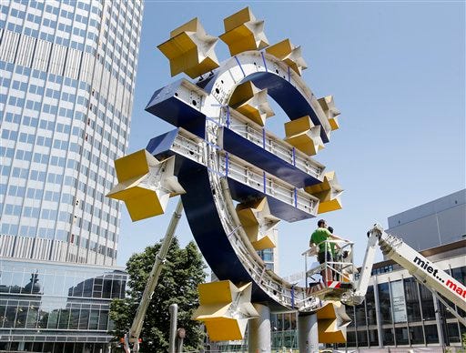 Two workers stand on a lifting platform during renovation works at the Euro sculpture in front of the old European Central Bank in Frankfurt, Germany, Monday, July 6, 2015. The sculpture will be renovated during the next four days. (AP Photo/Michael Probst)