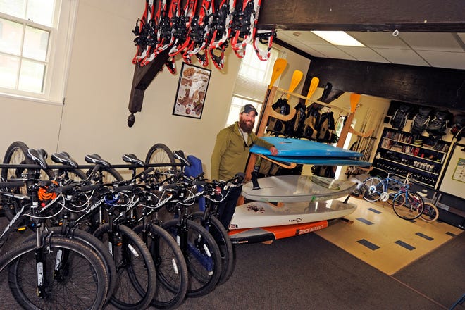 LSSU Regional Outdoor Center Director Paul Tumey poses with some of the many pieces of outdoor equipment for rent at the facility, including mountain bikes, stand-up paddleboards, snowshoes, backpacks, fishing gear, cross-country skis, and more. The ROC has been open to LSSU students for a year, but now Tumey is seeking to help others in the community enjoy the outdoors.
