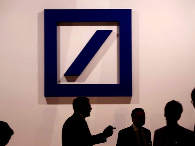 People are silhouetted as they stand near the logo of Deutsche Bank prior to the annual shareholders meeting in Frankfurt, Germany, Thursday, May 21, 2015.