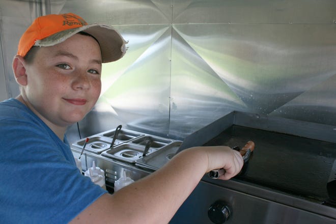 Max Jordan prepares a hot dog on his steam table in the College Dogs trailer on Main Street. Item photo/KEN CLEVELAND
