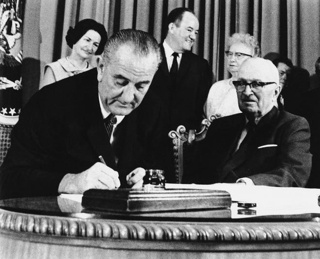 In this July 30, 1965 file photo, President Lyndon Johnson signs the Medicare Bill into law while former President Harry S. Truman, right, observes during a ceremony at the Truman Library in Independence, Mo. At rear are Lady Bird Johnson, Vice President Hubert Humphrey, and former first lady Bess Truman. When Johnson signed Medicare and Medicaid into law Americans 65 and older were the age group least likely to have health insurance. (AP Photo)