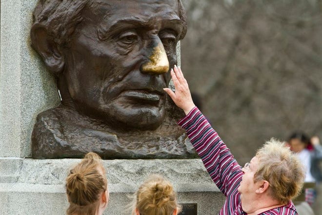 In this April 8, 2015, photo, a woman reaches up to rub the nose of an Abraham Lincoln bust outside his tomb in Springfield. Local legend says rubbing the nose brings good luck.