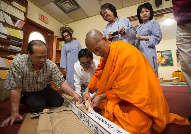 Ven. Thich Phouc Tri, abbot at Vietnamese Buddhist Temple, unwraps a Peace Pole from Rockford Interfaith Council on Sunday, Aug. 2, 2015, at the temple in Rockford. The pole has messages of peace in several languages. SUNNY STRADER/RRSTAR.COM