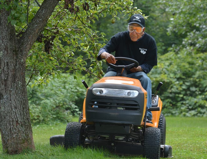 Richard Fiske, negotiating a rider mower around a tree in North Brookfield, still works every week: "I brought up the kids to mow lawns, play ball and shovel snow. I said if you do that and keep exercising, you'll live to be 90, and here I am 90." Photo/Chris Christo