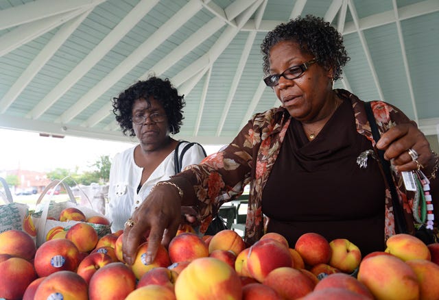 Vanessa Brunton, right, and Belinda Basden look through a pile of peaches while shopping at the Kinston-Lenoir County Farmer’s Market on Tuesday. This week marks National Farmer’s Market Week.