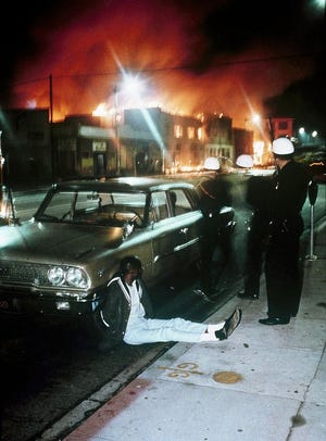 POLICE DETAIN A MAN as buildings burn during rioting that swept the Watts district of Los Angeles. It began with a routine traffic stop 50 years ago this month, blossomed into a protest with the help of a rumor and escalated into the deadliest and most destructive riot Los Angeles had seen.