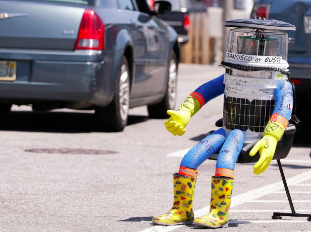 A car drives by HitchBOT, a hitchhiking robot Friday, July 17, 2015, in Marblehead, Mass. HitchBOT is beginning its' first cross-country hitchhiking trip of the U.S., in Marblehead with a final destination goal of reaching San Francisco. AP Photo/Stephan Savoia