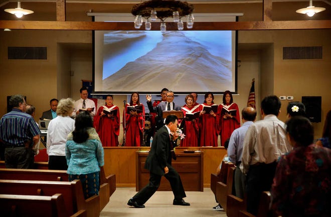 In a Sunday, Aug. 2, 2015 photo, Pastor Dr. Houmphanh Vongsurith, center, leans in to hush the children in the front row that were growing anxious while the choir sang during the bilingual (English and Lao) Sunday service at the First Laotian Baptist Church in Dallas. The church recently celebrated its 40th anniversary of Laotian refugees' migration to the U.S. Vongsurith was a prisoner of a brain washing camp for five years until he turned 21, when he escaped and somehow managed to make it to a Thailand refugee camp. The church serves as a bedrock for the small Laotian community that exists in Dallas Fort Worth. For the pastor, his faith gave him purpose in a life that was otherwise degraded by torture, suffering and loneliness. (Tom Fox/The Dallas Morning News via AP)