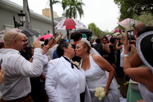 Alma Rosado,left, and Flor Maria Montijo, right, kiss after their wedding during a mass same-sex wedding in San Juan, Puerto Rico, Sunday, Aug. 16, 2015. Over 60 couples from around the region gathered in Puerto Rico"™s capital to exchange vows at a same-sex marriage ceremony. (AP Photo/Ricardo Arduengo)