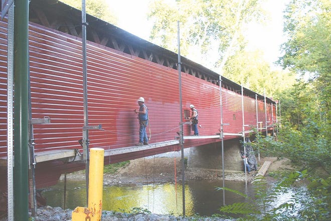 Mike Vonada, left, and Austin Tressler use a sprayer and a brush to paint the siding of Martins Mill Bridge.