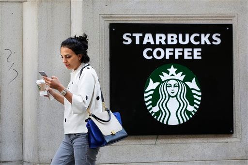 FILE- In this July 16, 2015, file photo, a woman walks out of a Starbucks Coffee with a beverage in hand in New York. Starbucks and Panera are each hyping reformulated versions of their pumpkin spice lattes in a fight to win over fans of the drink in coming weeks. Starbucks Corp. said Monday, Aug. 17, its version of the concoction this year will be made with real pumpkin, and without caramel coloring. (AP Photo/Mark Lennihan, File)